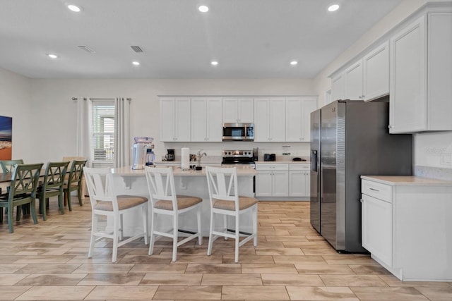 kitchen with white cabinetry, a center island with sink, a kitchen breakfast bar, and appliances with stainless steel finishes