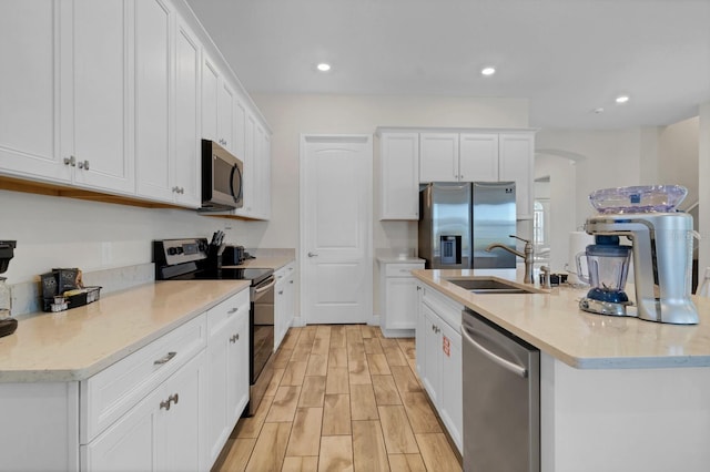 kitchen featuring sink, stainless steel appliances, light stone counters, an island with sink, and white cabinets