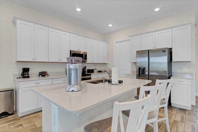 kitchen featuring an island with sink, appliances with stainless steel finishes, white cabinets, and a kitchen bar