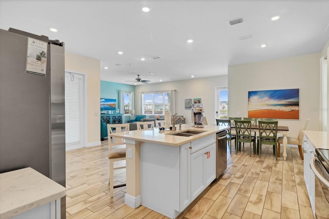 kitchen with appliances with stainless steel finishes, sink, white cabinets, ceiling fan, and a center island with sink