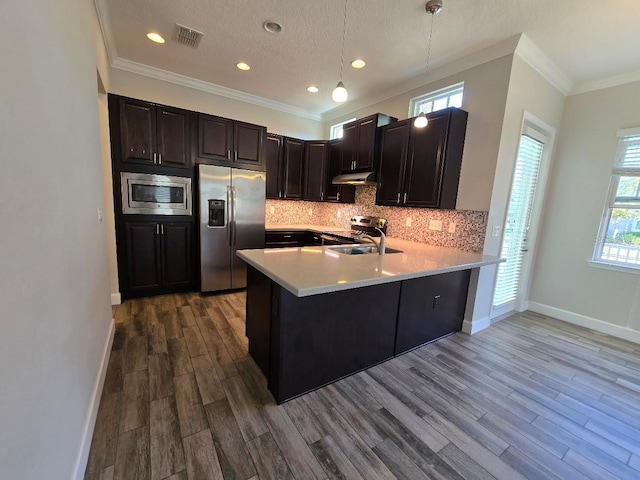 kitchen with appliances with stainless steel finishes, hardwood / wood-style floors, tasteful backsplash, decorative light fixtures, and kitchen peninsula