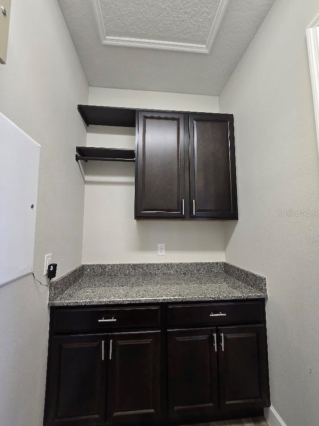 kitchen featuring dark brown cabinetry, stone counters, and a textured ceiling