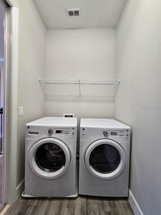 clothes washing area with independent washer and dryer, dark hardwood / wood-style floors, and a textured ceiling