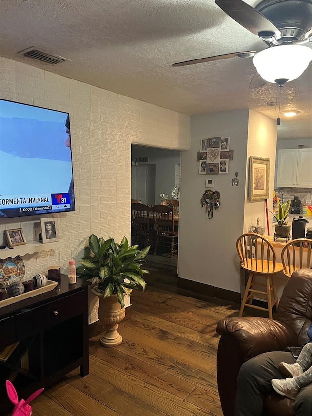 living room featuring wood-type flooring, a textured ceiling, and ceiling fan