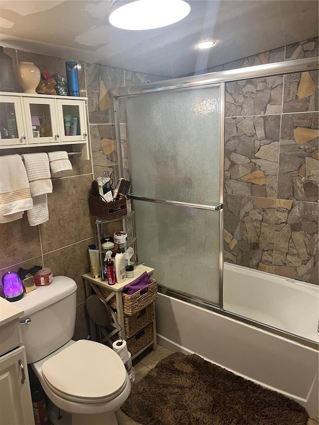 full bathroom featuring tile walls, combined bath / shower with glass door, vanity, and toilet