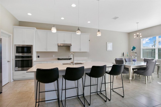 kitchen featuring oven, hanging light fixtures, a kitchen island with sink, sink, and white cabinets