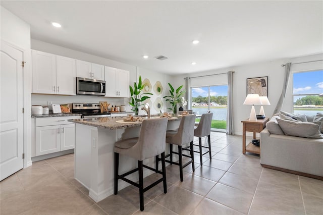 kitchen featuring white cabinets, stainless steel appliances, an island with sink, stone counters, and a breakfast bar area