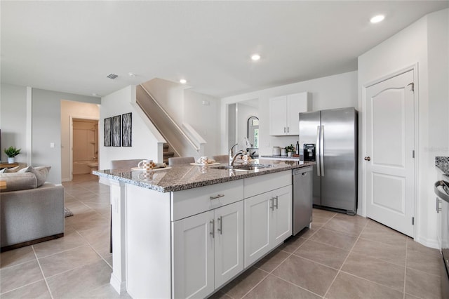 kitchen with light tile patterned floors, stainless steel appliances, a kitchen island with sink, light stone countertops, and white cabinets