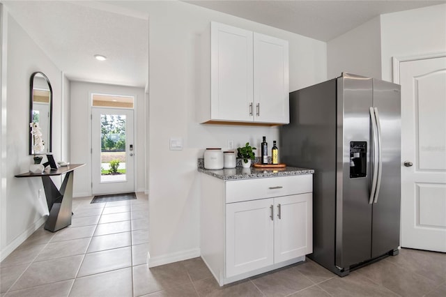 kitchen with stainless steel fridge with ice dispenser, light tile patterned floors, white cabinets, and dark stone counters