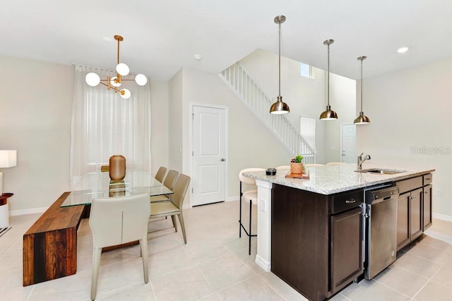 kitchen with decorative light fixtures, light stone counters, stainless steel dishwasher, and an island with sink