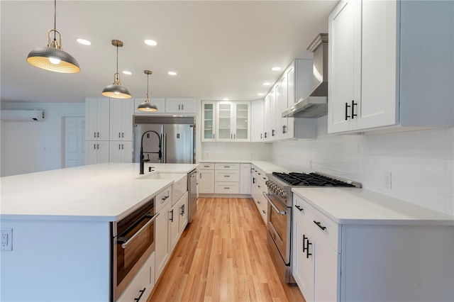 kitchen featuring high quality appliances, white cabinetry, pendant lighting, and wall chimney exhaust hood