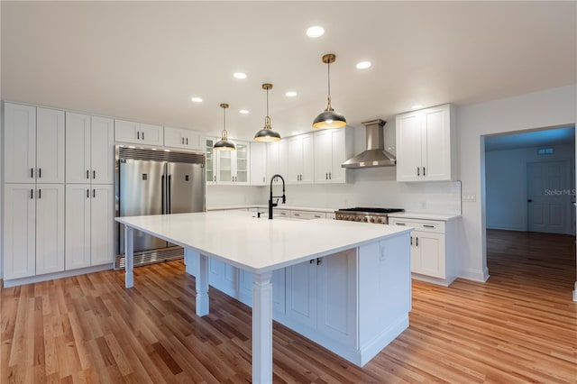 kitchen with pendant lighting, wall chimney range hood, white cabinetry, a kitchen breakfast bar, and stainless steel built in refrigerator