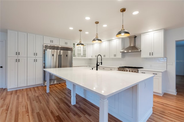 kitchen featuring wall chimney exhaust hood, sink, appliances with stainless steel finishes, light hardwood / wood-style floors, and white cabinets