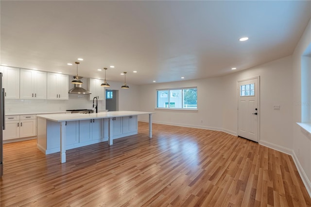 kitchen with white cabinets, decorative light fixtures, light wood-type flooring, and wall chimney range hood