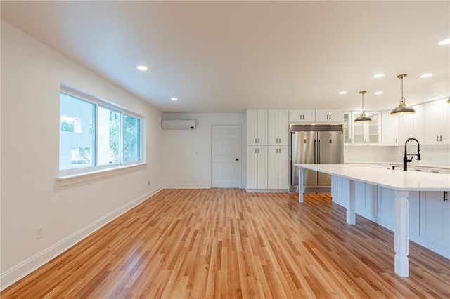 kitchen with pendant lighting, sink, built in refrigerator, a wall mounted AC, and white cabinets