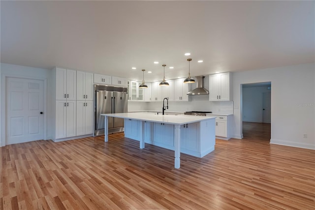 kitchen with pendant lighting, white cabinetry, wall chimney exhaust hood, and stainless steel built in fridge