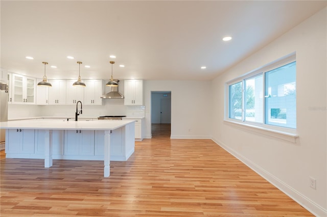 kitchen with sink, white cabinetry, hanging light fixtures, light hardwood / wood-style floors, and wall chimney exhaust hood