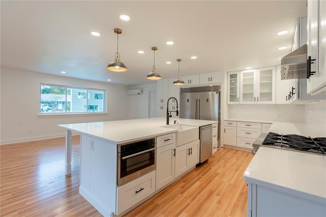 kitchen featuring white cabinetry, decorative light fixtures, appliances with stainless steel finishes, and a center island with sink