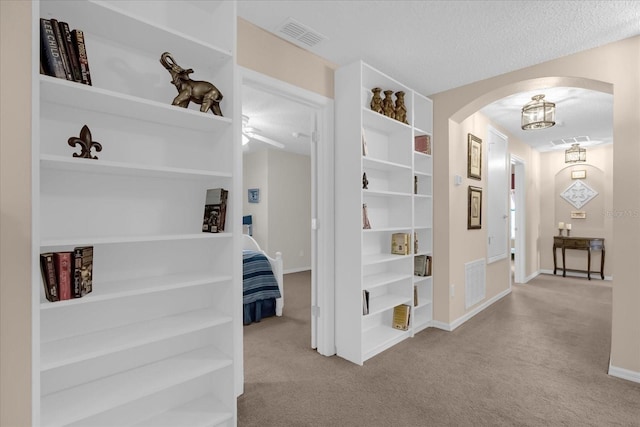 corridor with light carpet and a textured ceiling