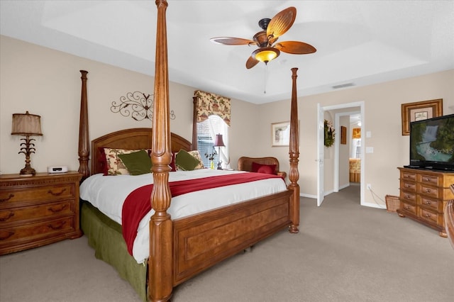 bedroom featuring ceiling fan, a tray ceiling, and light carpet