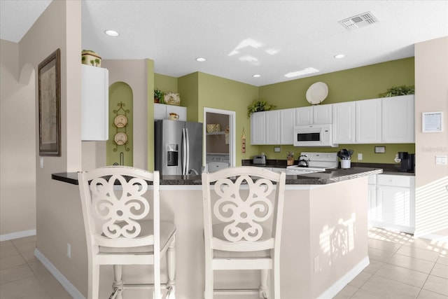 kitchen featuring white cabinets, a kitchen bar, light tile patterned floors, white appliances, and a textured ceiling