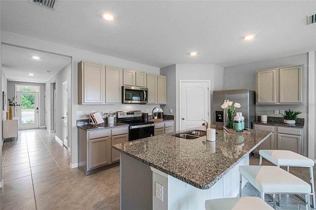 kitchen with a breakfast bar, sink, an island with sink, stainless steel appliances, and dark stone counters