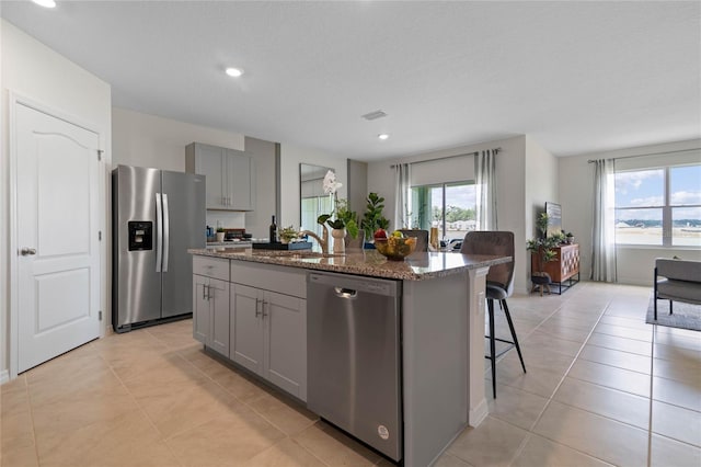 kitchen with a center island with sink, a breakfast bar area, appliances with stainless steel finishes, gray cabinetry, and dark stone counters