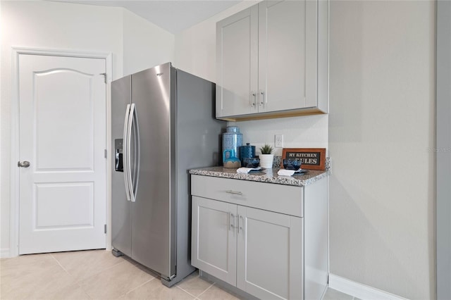 kitchen with stainless steel refrigerator with ice dispenser, light stone counters, light tile patterned floors, and gray cabinetry