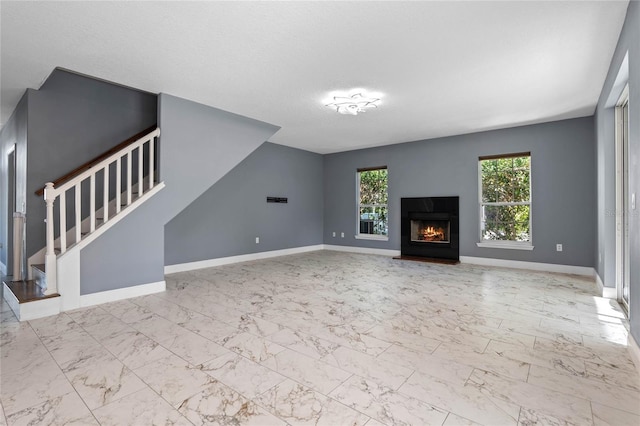 unfurnished living room with marble finish floor, a warm lit fireplace, stairs, and baseboards