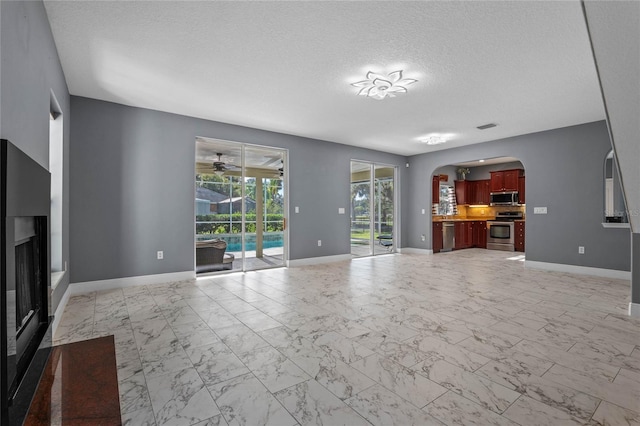 unfurnished living room featuring arched walkways, a textured ceiling, a fireplace, baseboards, and marble finish floor