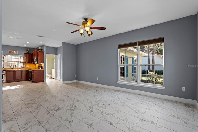 unfurnished living room featuring a ceiling fan, marble finish floor, and baseboards