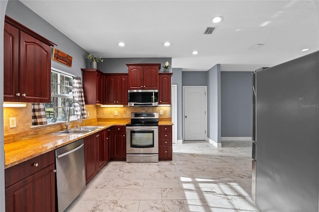 kitchen featuring a sink, marble finish floor, dark brown cabinets, appliances with stainless steel finishes, and decorative backsplash