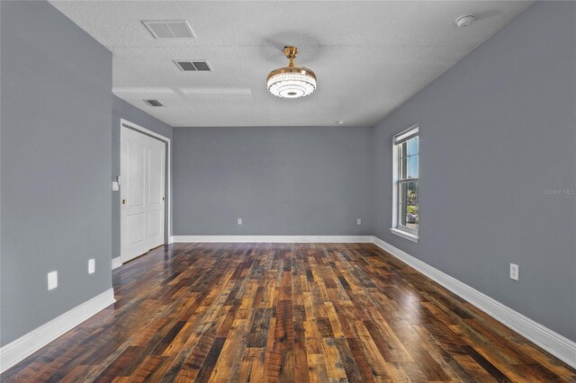 empty room featuring wood-type flooring, visible vents, a textured ceiling, and baseboards