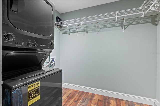 clothes washing area featuring laundry area, baseboards, stacked washer / drying machine, and wood finished floors