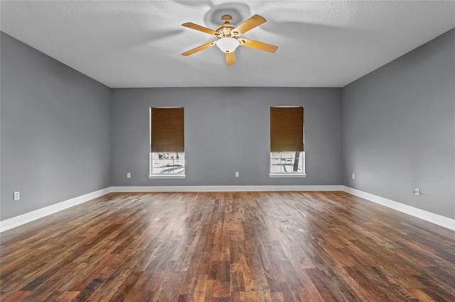 empty room with a textured ceiling, dark wood finished floors, a ceiling fan, and baseboards