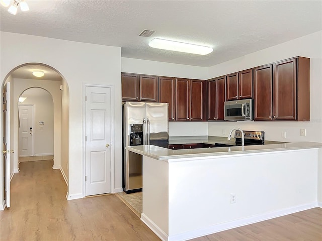 kitchen with stainless steel appliances, a textured ceiling, light hardwood / wood-style floors, and kitchen peninsula