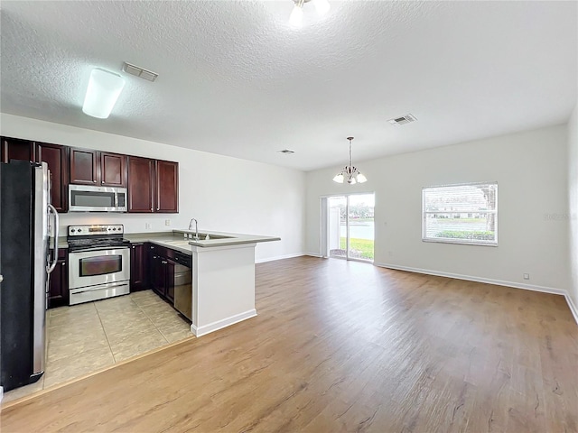 kitchen with sink, light wood-type flooring, appliances with stainless steel finishes, kitchen peninsula, and pendant lighting