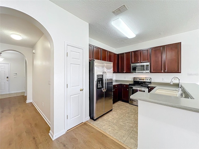 kitchen featuring stainless steel appliances, sink, a textured ceiling, and light hardwood / wood-style flooring