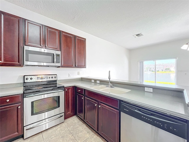 kitchen featuring sink, a textured ceiling, light tile patterned floors, kitchen peninsula, and stainless steel appliances