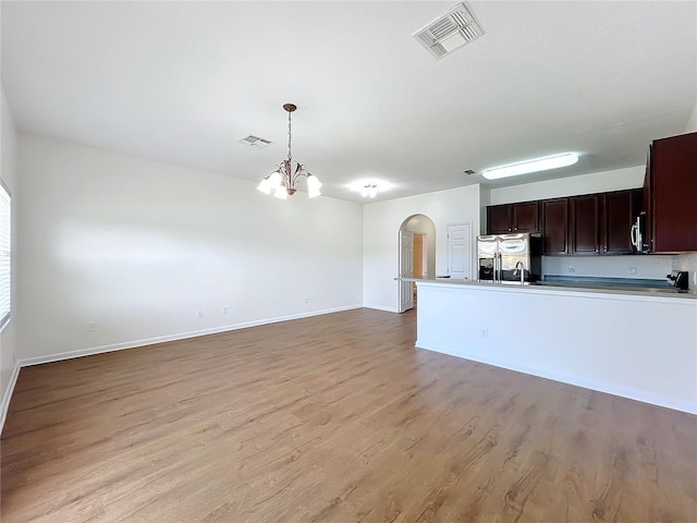 kitchen with hanging light fixtures, a notable chandelier, stainless steel appliances, dark brown cabinets, and light hardwood / wood-style flooring