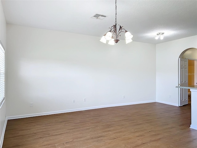 unfurnished room featuring dark wood-type flooring, a notable chandelier, a textured ceiling, and a wealth of natural light