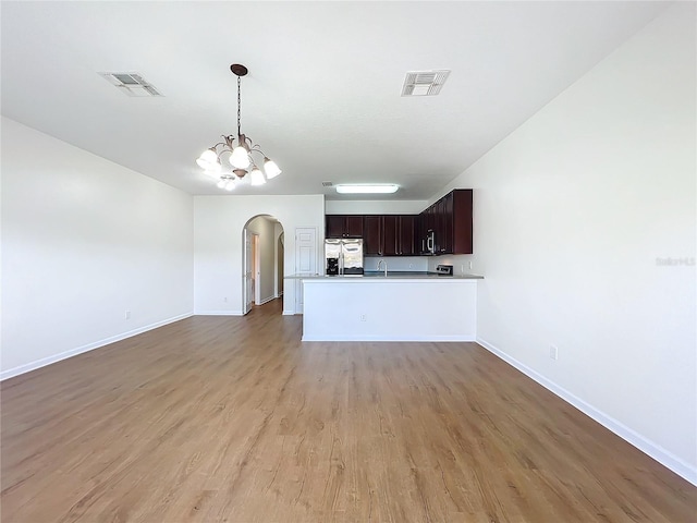 kitchen with stainless steel refrigerator with ice dispenser, dark brown cabinetry, a notable chandelier, kitchen peninsula, and light wood-type flooring