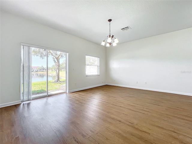 empty room with dark hardwood / wood-style flooring, a water view, a textured ceiling, and an inviting chandelier