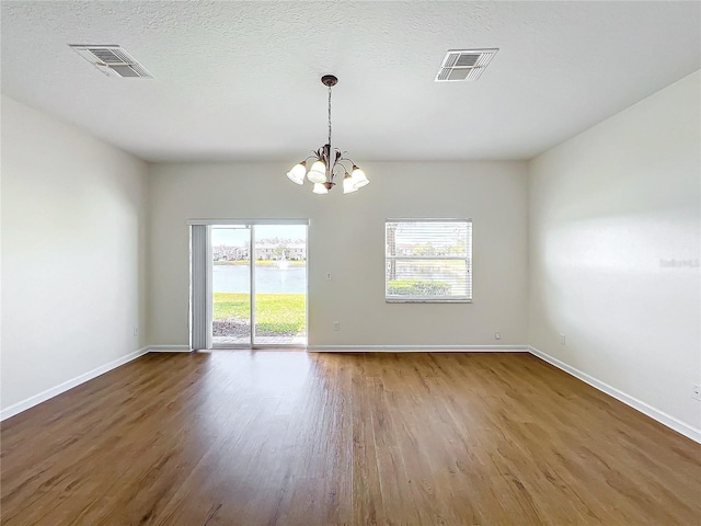 empty room with a chandelier, hardwood / wood-style floors, and a textured ceiling