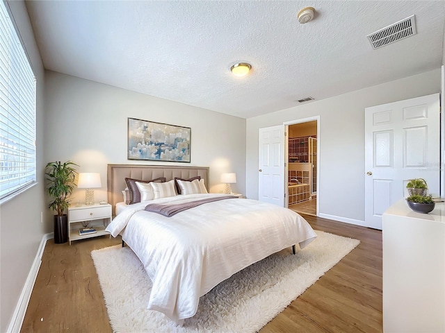 bedroom with ensuite bath, dark wood-type flooring, and a textured ceiling