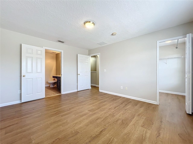 unfurnished bedroom with connected bathroom, a spacious closet, a textured ceiling, light wood-type flooring, and a closet