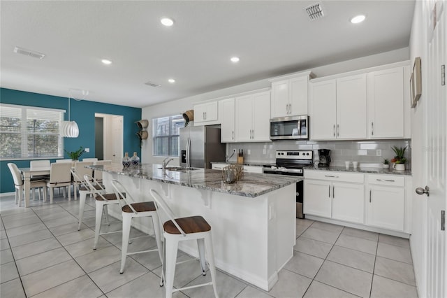 kitchen with an island with sink, white cabinets, tasteful backsplash, and stainless steel appliances