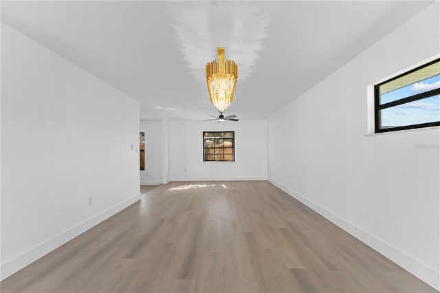 unfurnished room featuring ceiling fan with notable chandelier, plenty of natural light, and light wood-type flooring