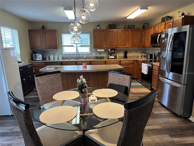 kitchen featuring a center island, appliances with stainless steel finishes, decorative backsplash, sink, and decorative light fixtures