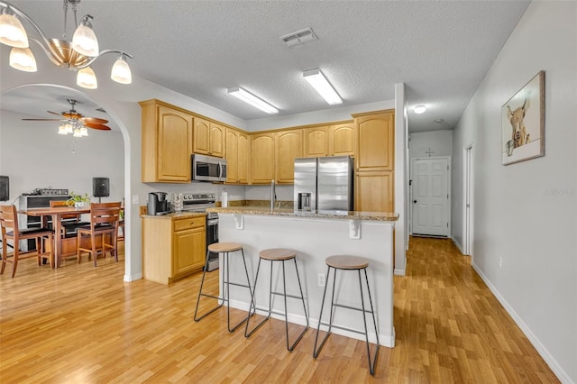 kitchen with ceiling fan, stainless steel appliances, a textured ceiling, a kitchen island, and light stone counters